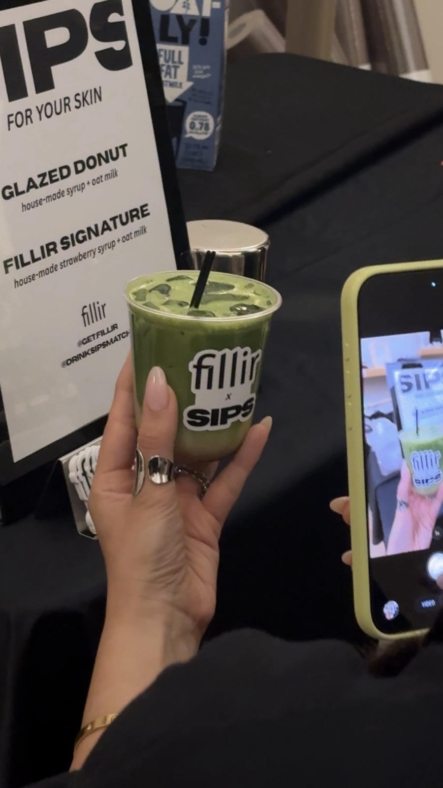 A Fillir × SIPS matcha held up next to the Glazed Donut and Fillir Signature menu sign
